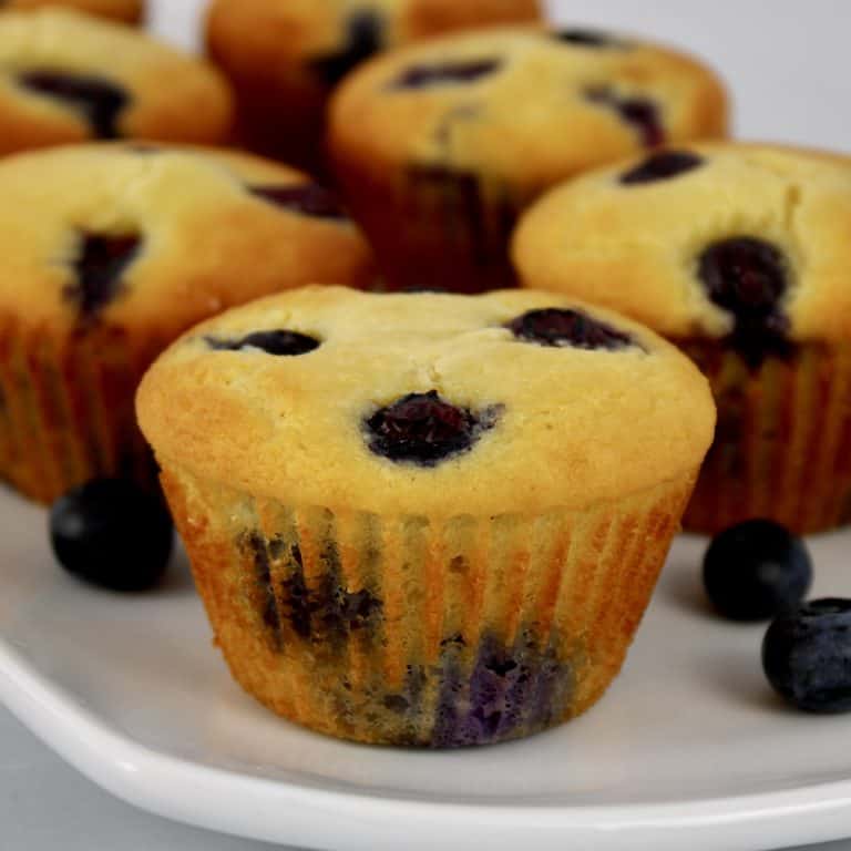 blueberry muffins on white plate with blueberries around