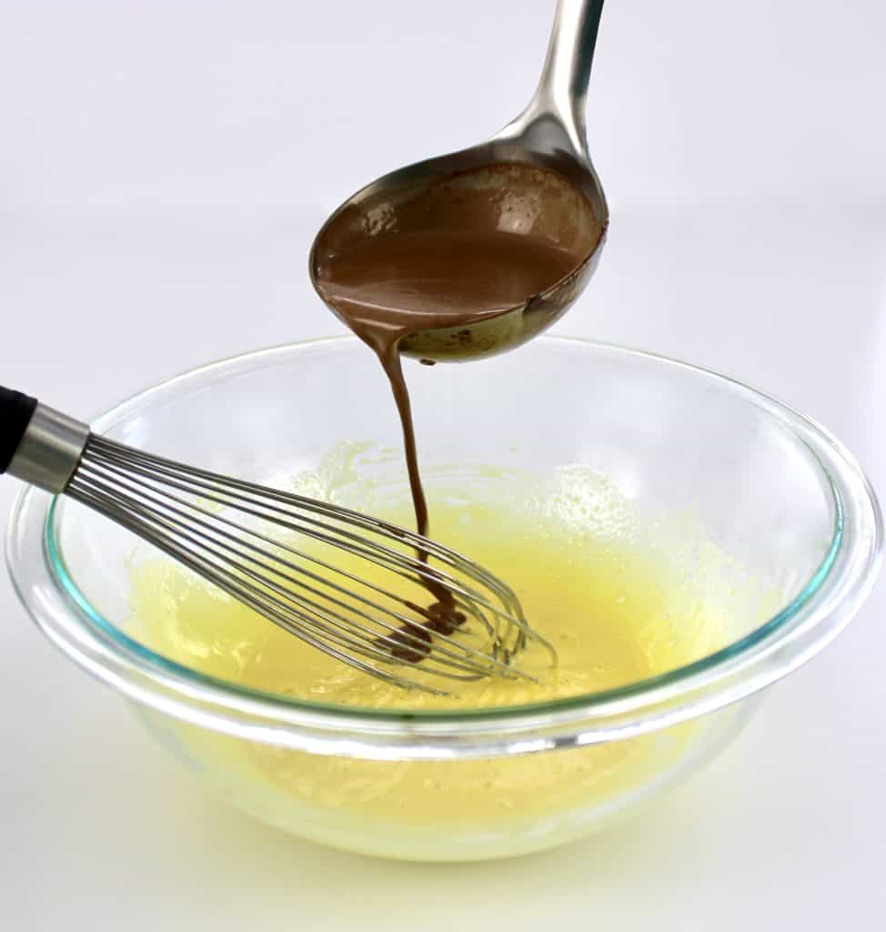 chocolate mixture being ladled in egg yolks bowl with whisk