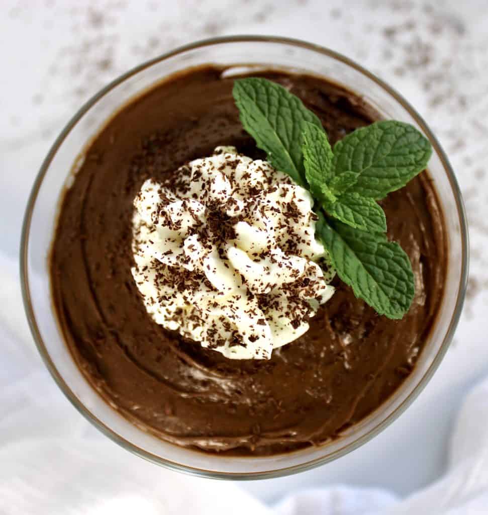 overhead view of chocolate pudding in glass bowl with whip cream and mint sprig on top