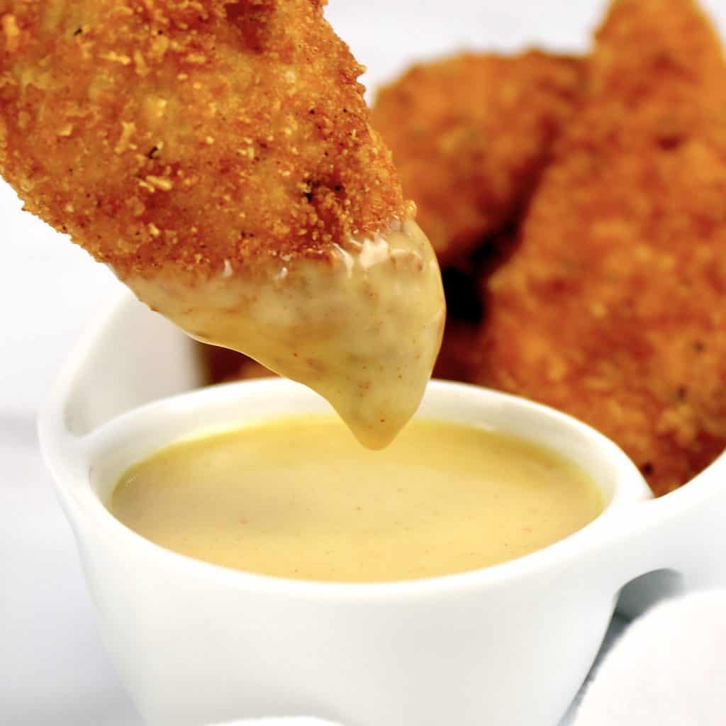 chicken tender being dipped into honey mustard