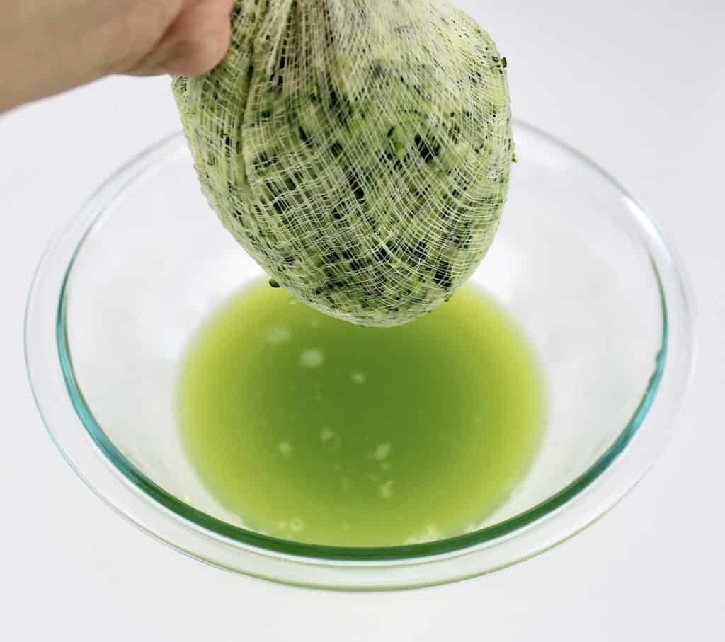 cheesecloth draining zucchini over glass bowl with green liquid
