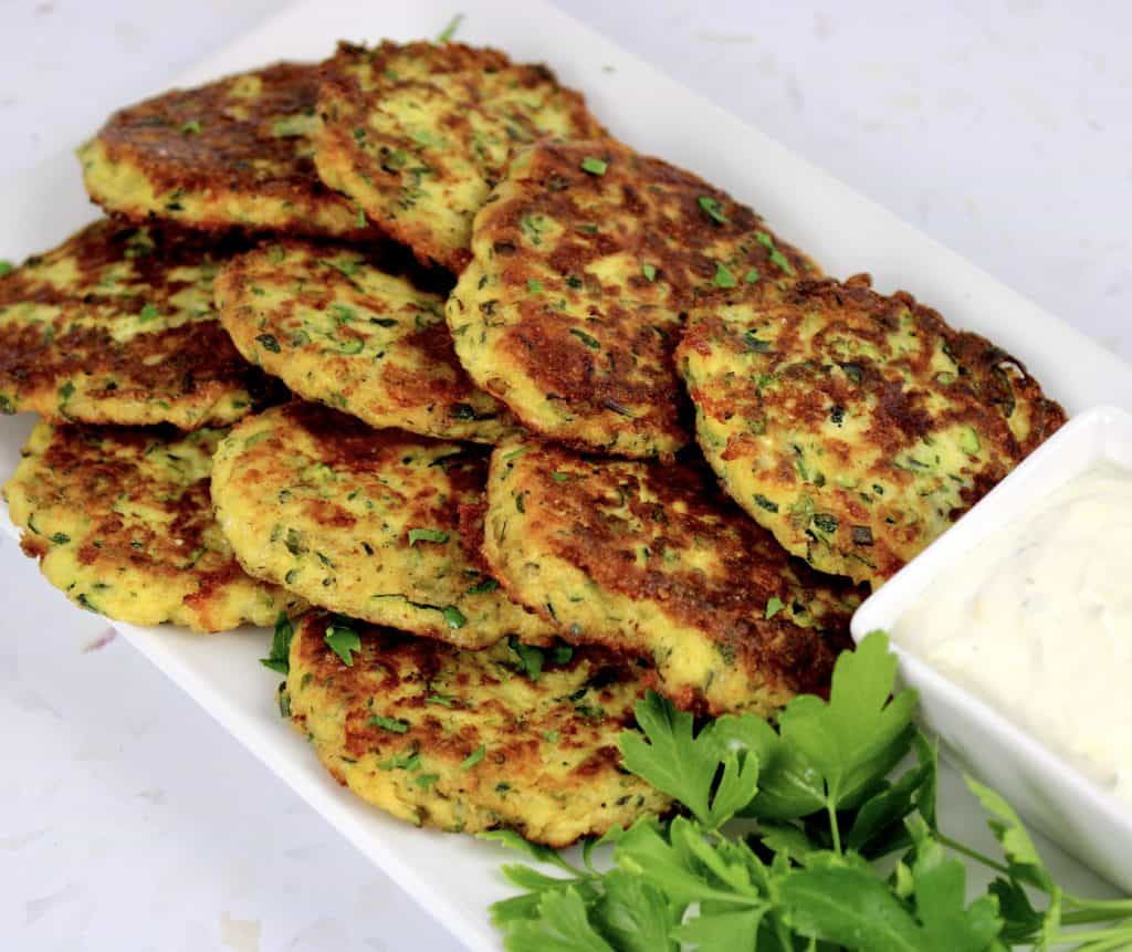 zucchini fritters piled up on white plate with dipping sauce