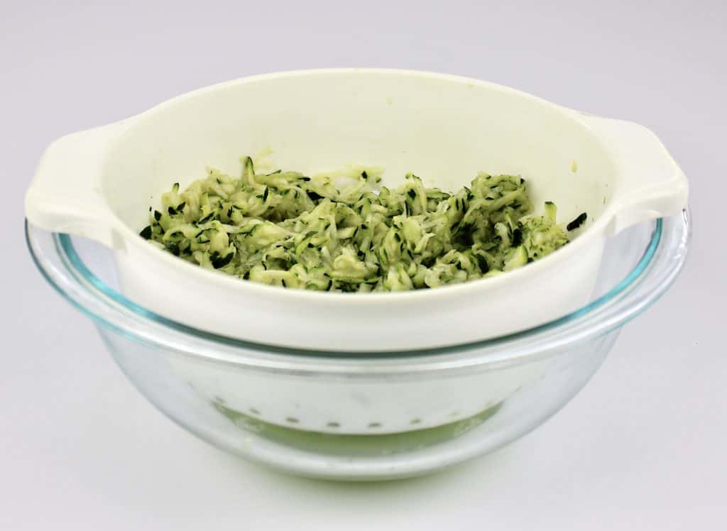 white colander with grated zucchini over glass bowl