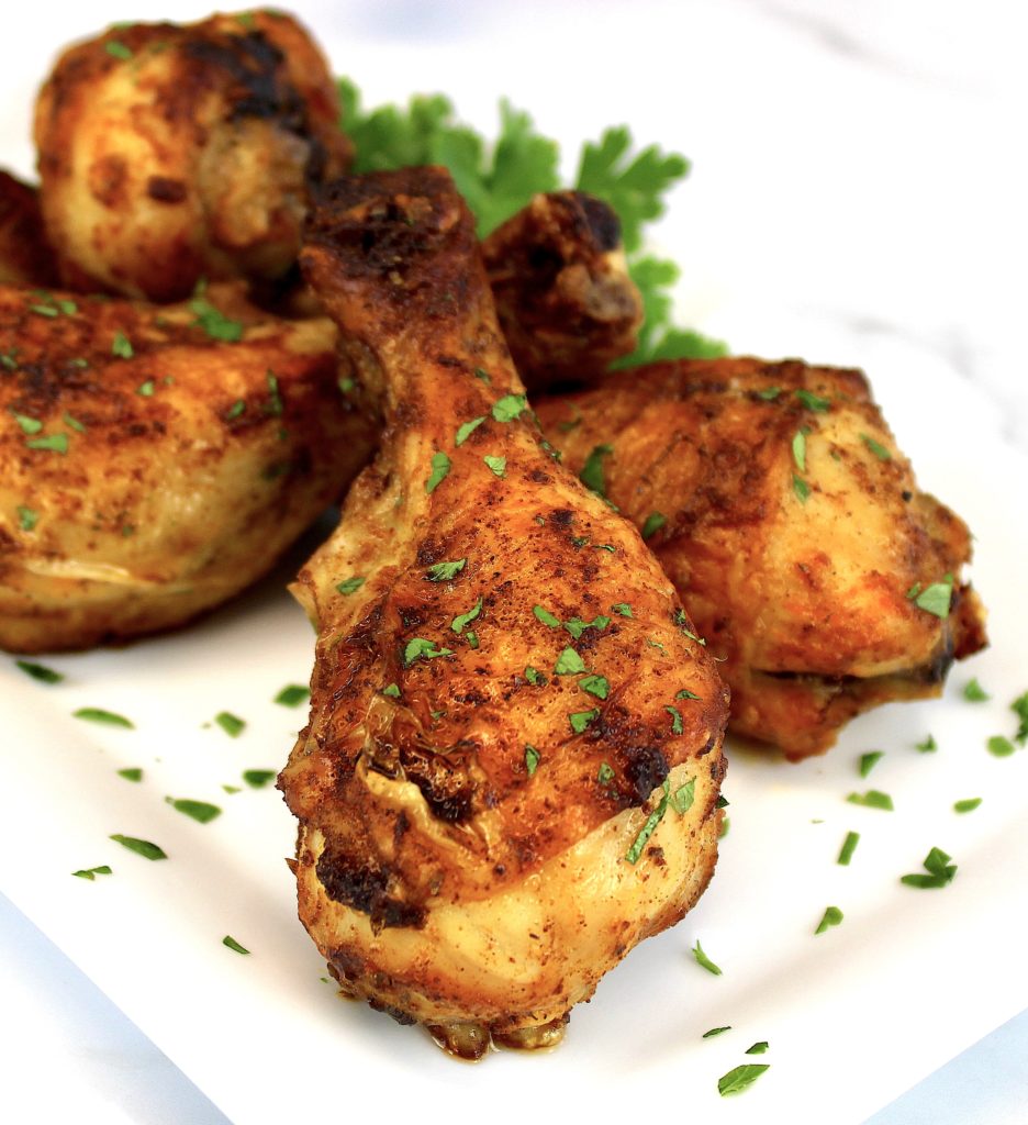 closeup of chicken legs on white plate with parsley garnish