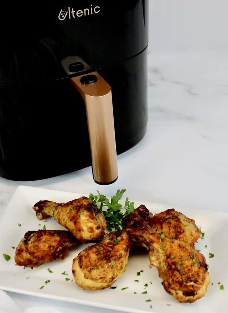 cooked chicken legs on white plate with Ultenic air fryer in background