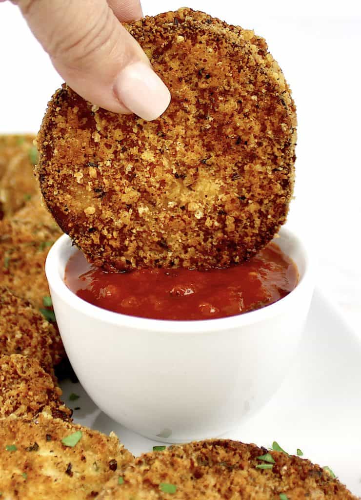 fried eggplant being dipped into marinara sauce in white cup