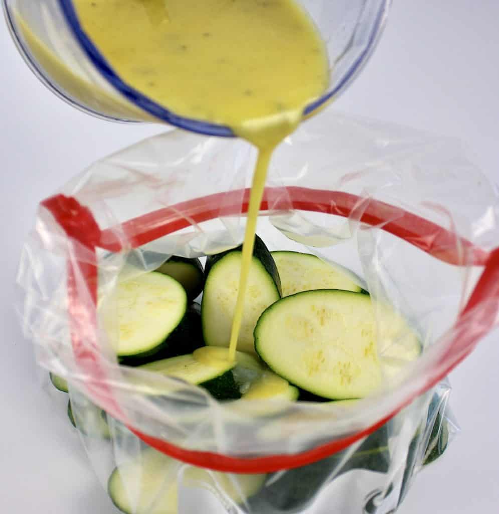 zucchini slices in ziploc bad with lemon dressing being poured over top