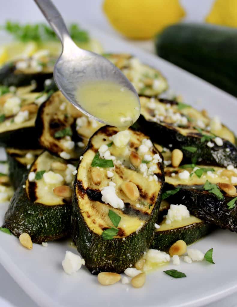 grilled zucchini slices with lemon dressing being spooned over top