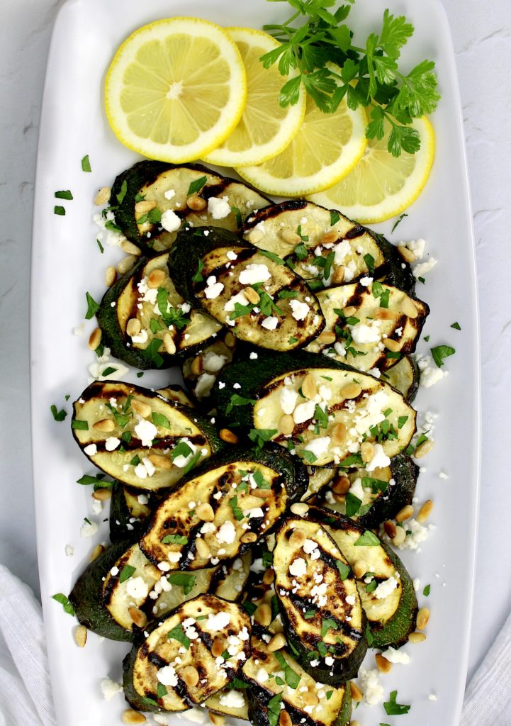 overhead view of grilled zucchini slices with feta pine nuts and lemon slices