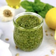 closeup of pesto sauce in open glass jar with lemons and basil in background