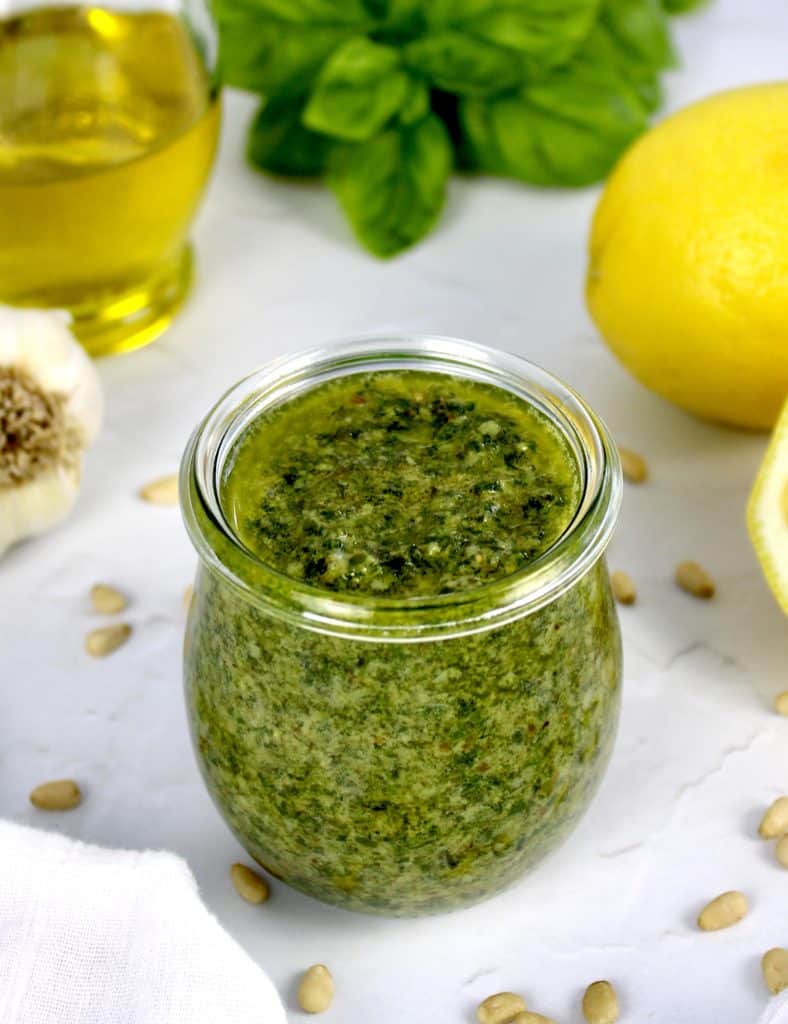 pesto sauce in open glass jar with lemon and basil in background