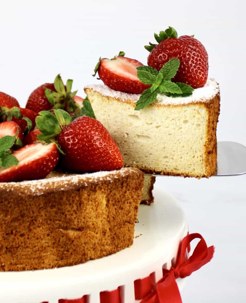slice of angel food cake with strawberries on top being removed from cake stand