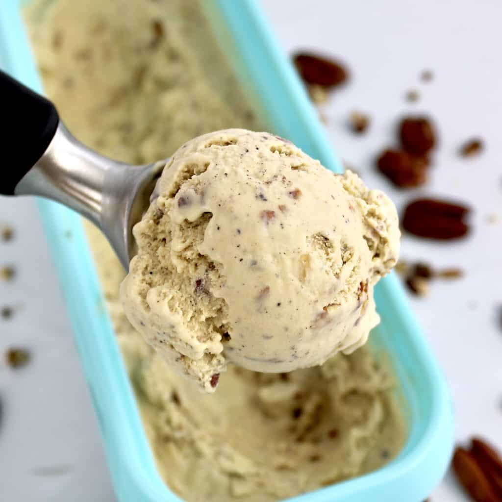 scoop of Keto Butter Pecan Ice Cream over turquoise container pecans in background