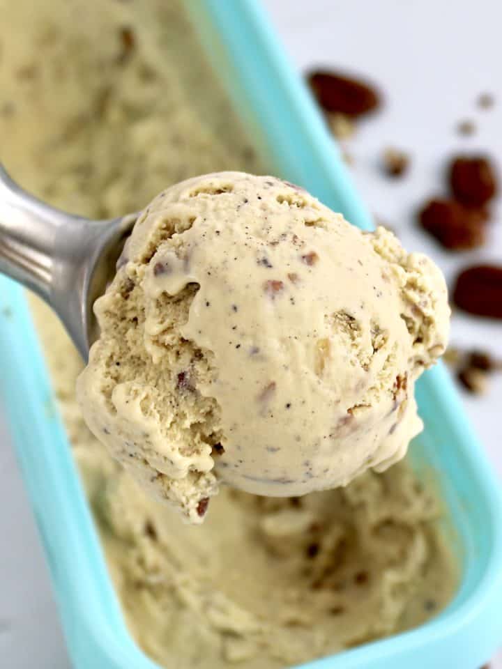 scoop of Keto Butter Pecan Ice Cream over turquoise container pecans in background