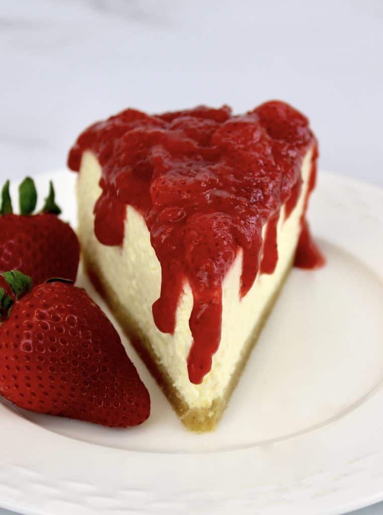 slice of cheesecake with strawberry sauce dripping down the sides