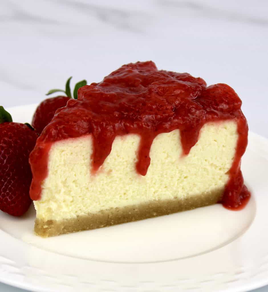 closeup of side of cheesecake slice with strawberry sauce dripping down the side