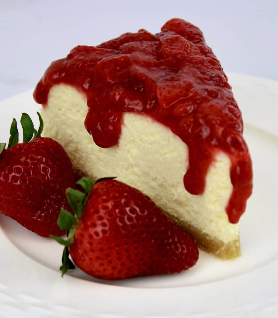 slice of cheesecake with chunky strawberry sauce dripping down sides