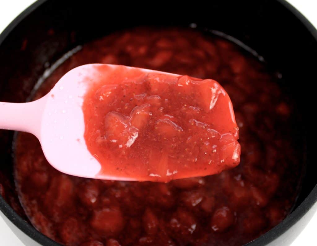strawberry sauce in pan with pink spoon holding up some