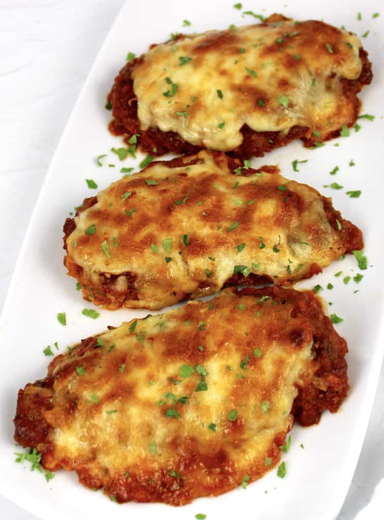 3 pieces of chicken parmesan on white plate with parsley on top