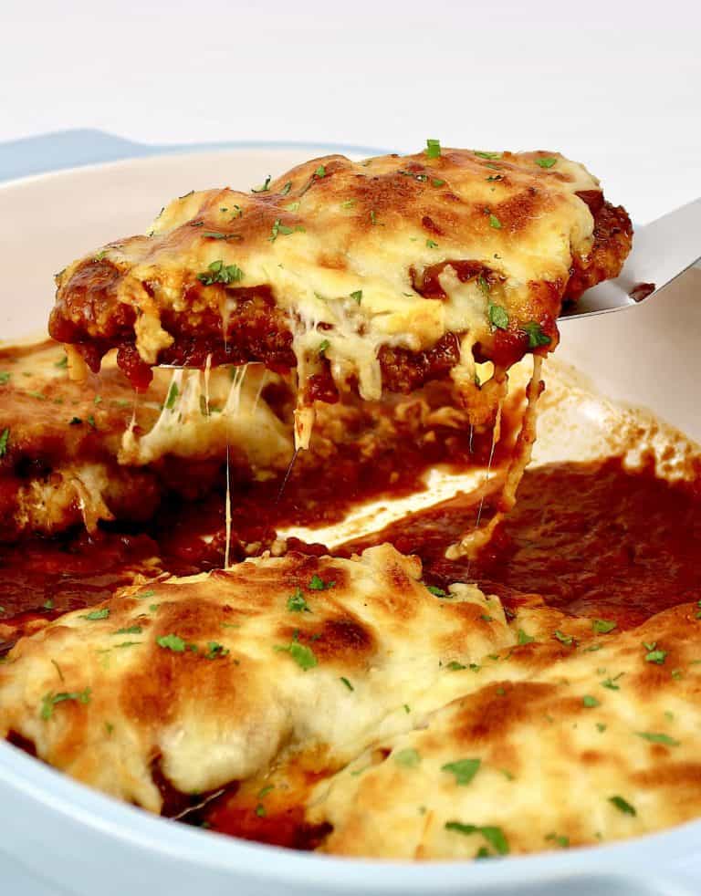 piece of chicken parmesan being lifted out of casserole dish