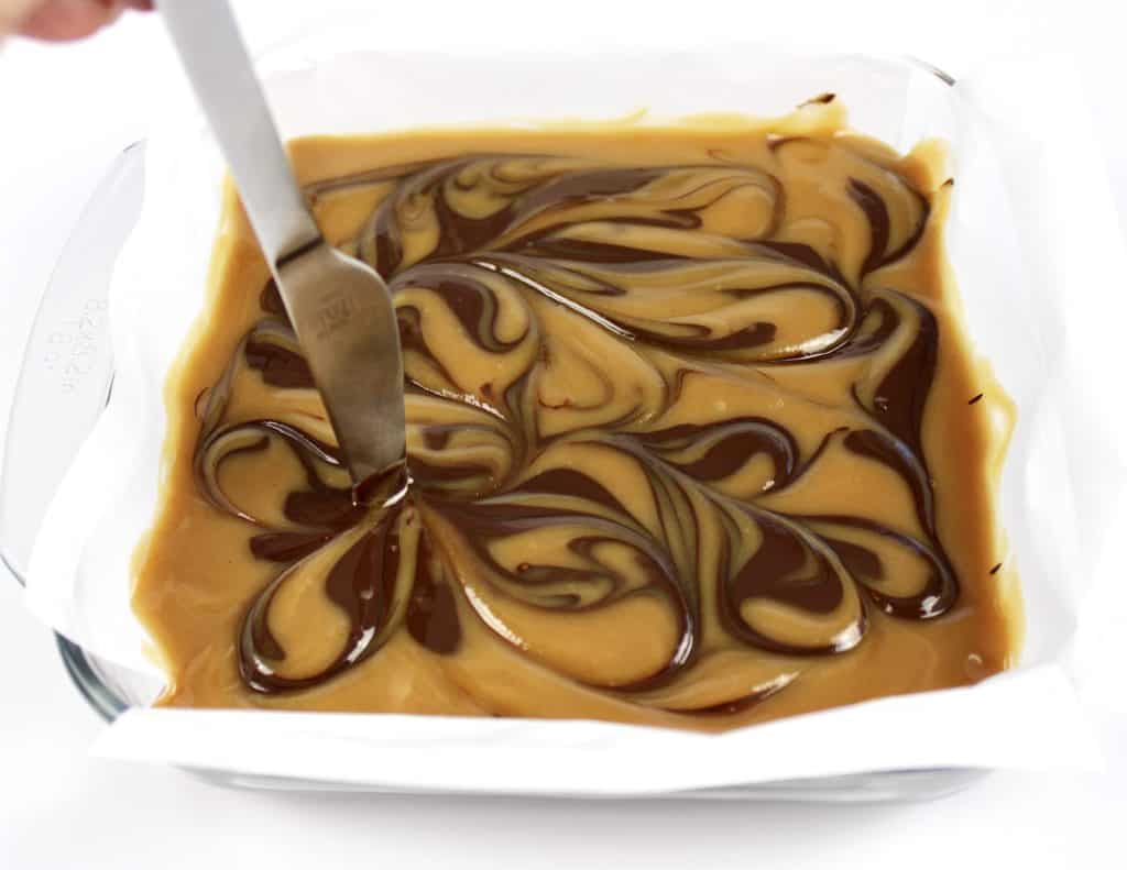 peanut butter fudge in baking dish with knife swirling chocolate through it