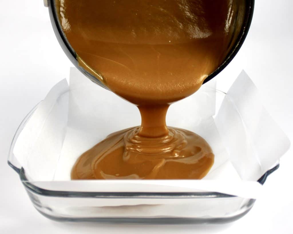 peanut butter fudge batter being poured from pan into glass dish with parchment paper
