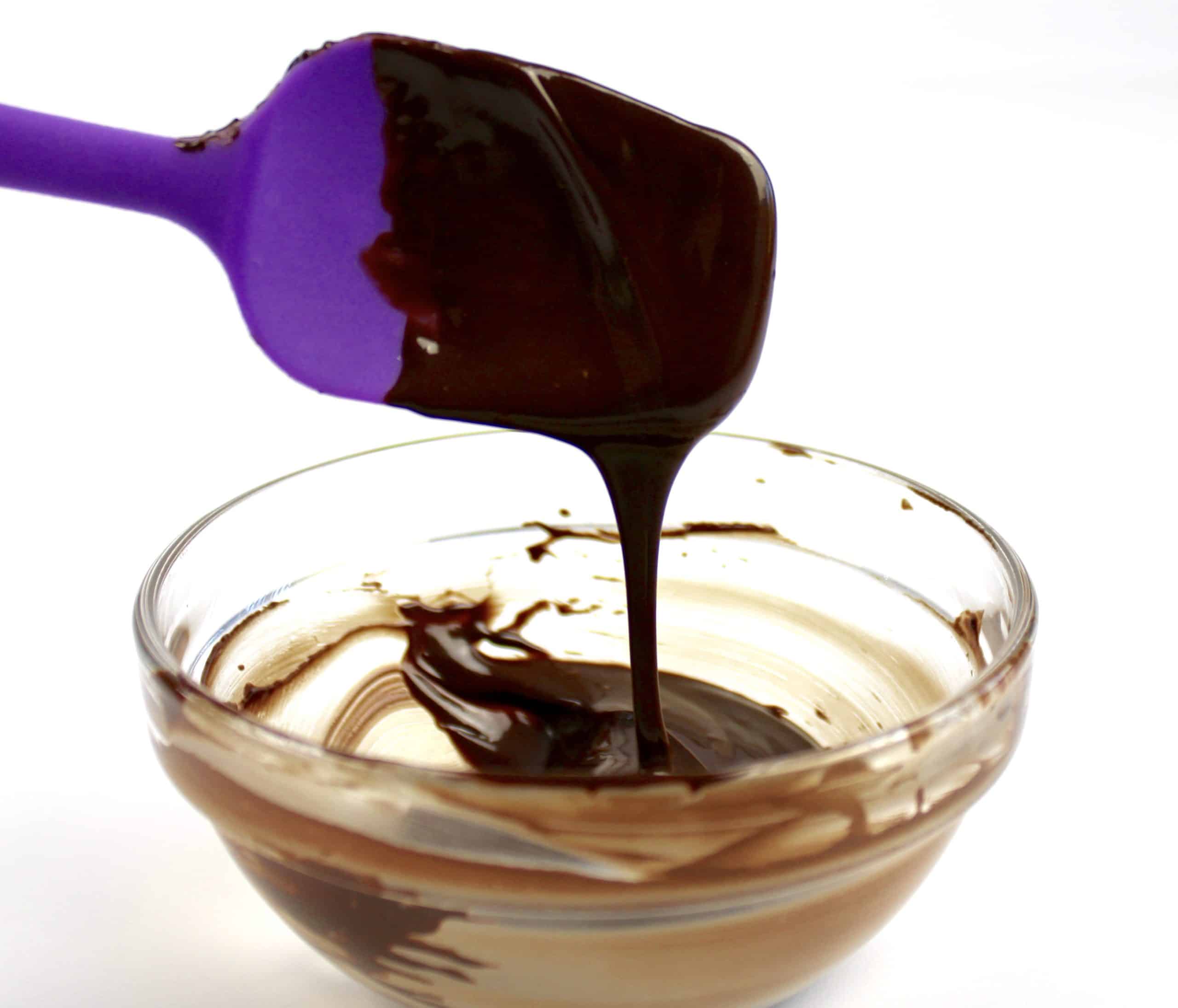melted chocolate in glass bowl with purple spatula dripping