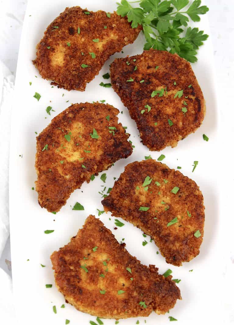 overhead view of 5 pork chops on white plate with parsley garnish