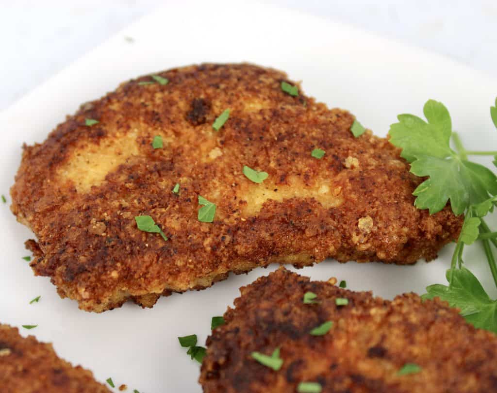 closeup of fried pork chop on white plate with chopped parsley