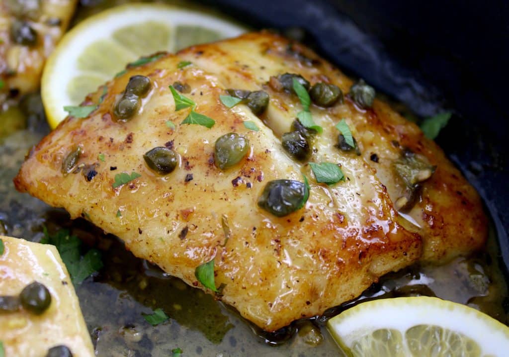 closeup of snapper in skillet with caper sauce and lemon slices