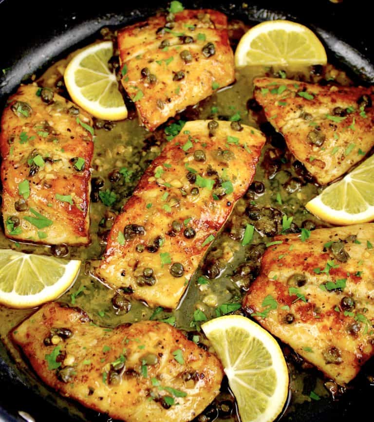 pieces of red snapper with lemon caper sauce in skillet with lemon slices