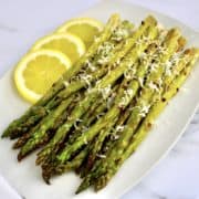 cooked asparagus on white plate with grated cheese on top 3 lemon slices on side