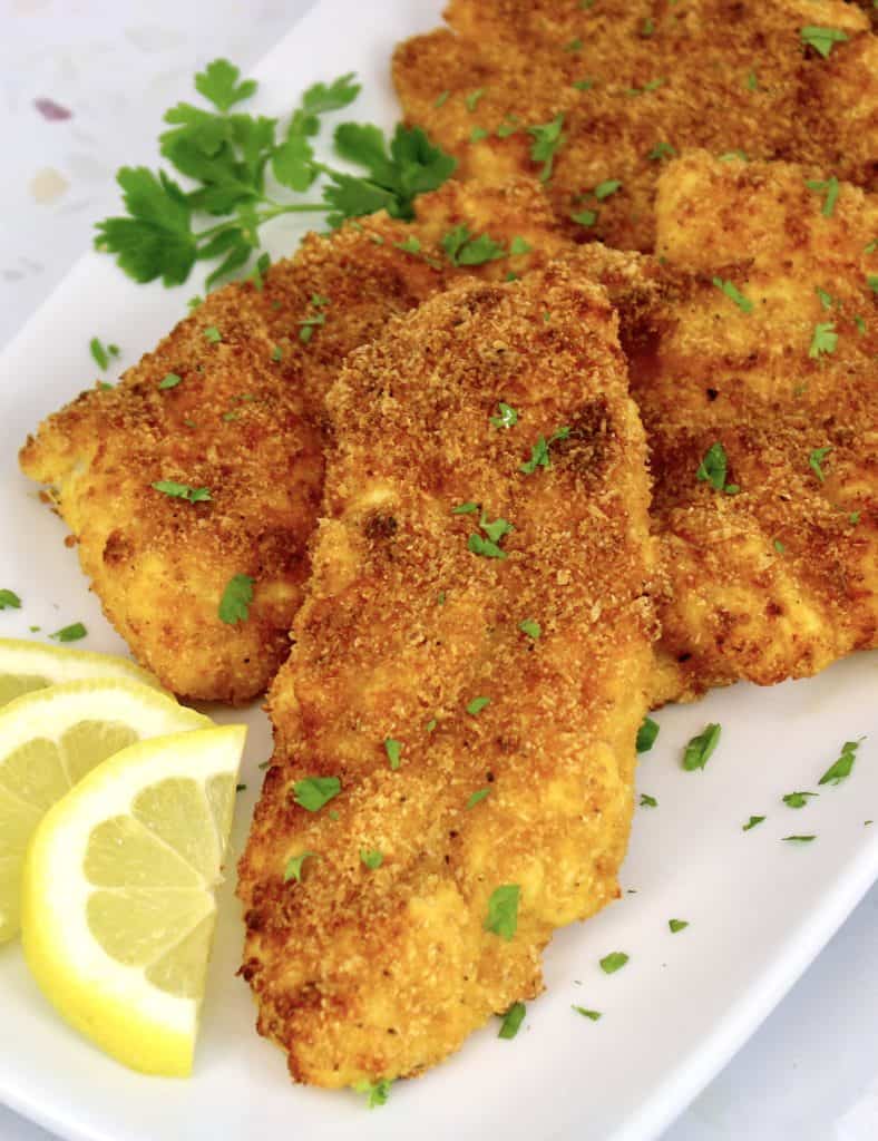 fried cod pieces on white plate with lemon slices and parsley garnish