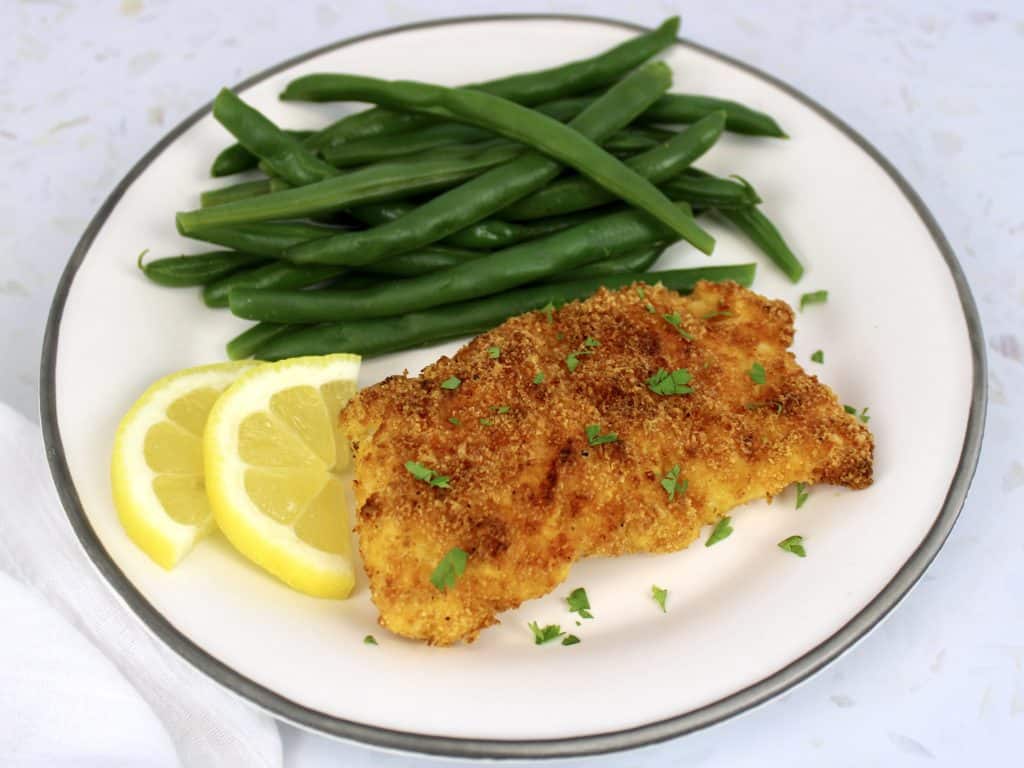 piece of fried fish with green beans on white plate with lemon slices