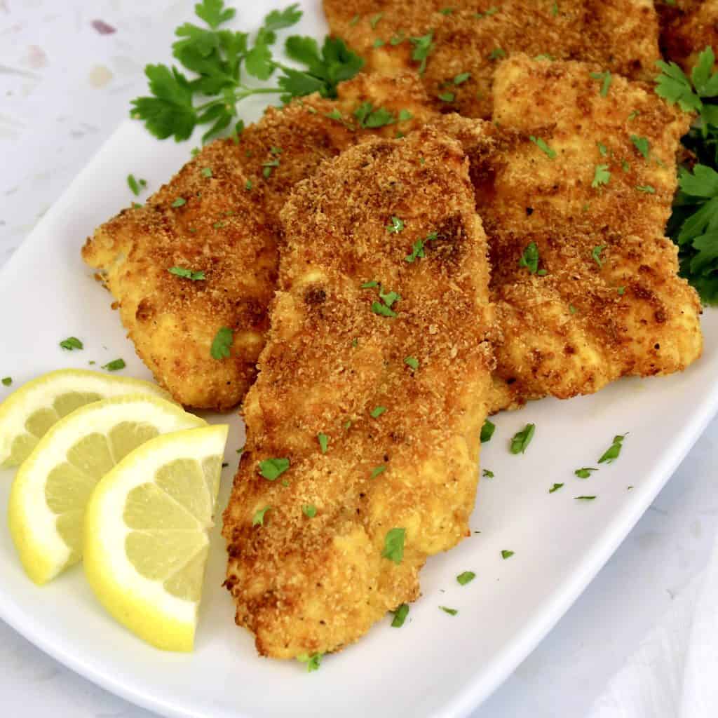 fried cod pieces on white plate with lemon slices and parsley garnish