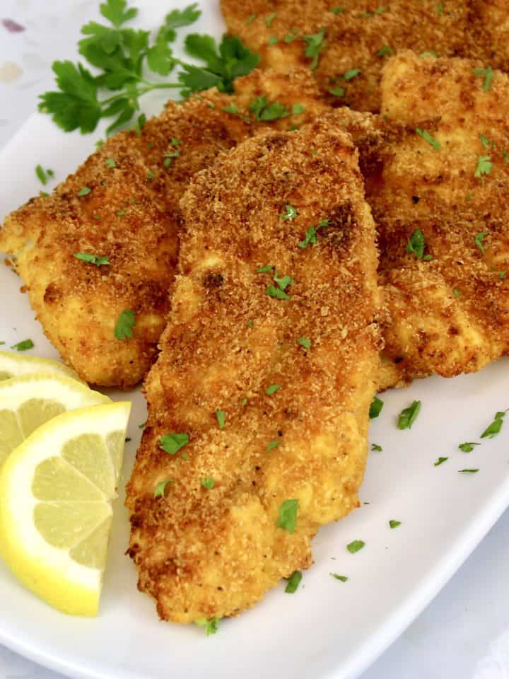 fried cod pieces on white plate with lemon slices and parsley garnish
