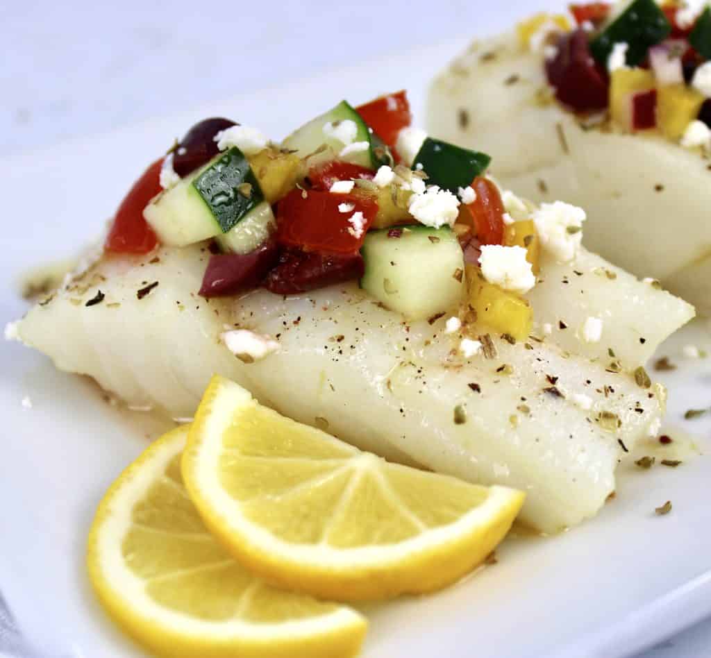 piece of cod with salsa on top with lemon slices on side