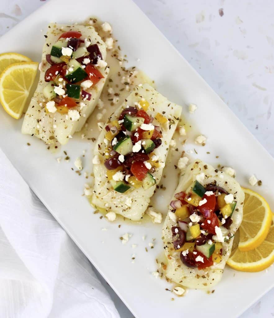 overhead view of 3 slices of cod with Greek salsa on top with lemon slices on sides