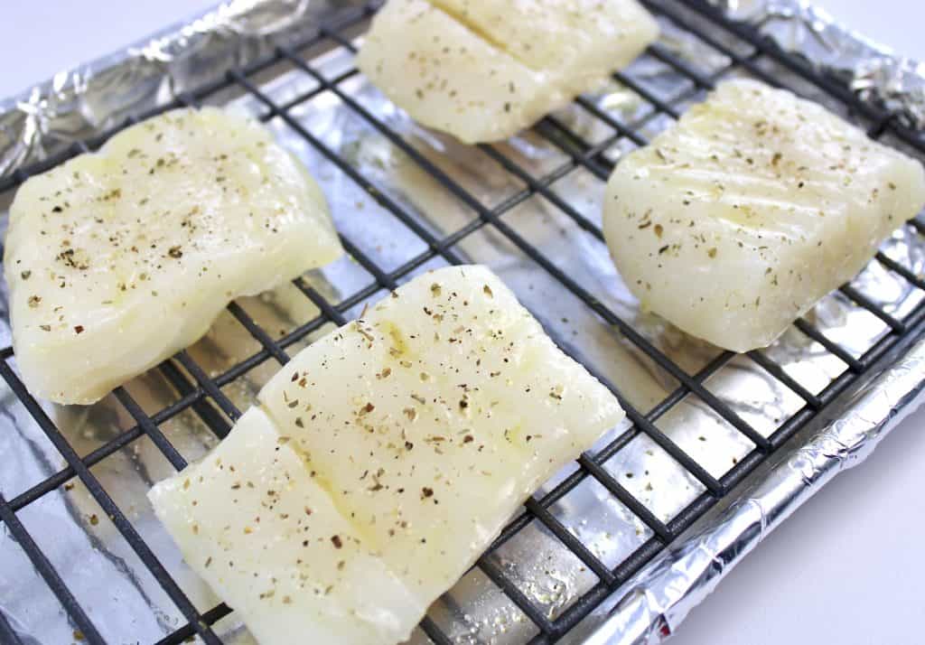 4 pieces of raw cod on baking rack with spices on top