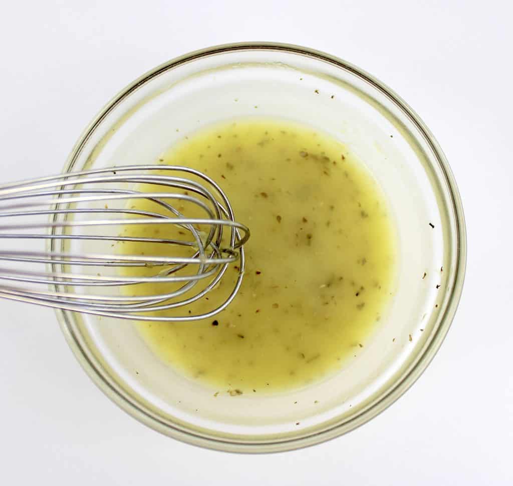 lemon olive oil dressing in glass bowl with whisk