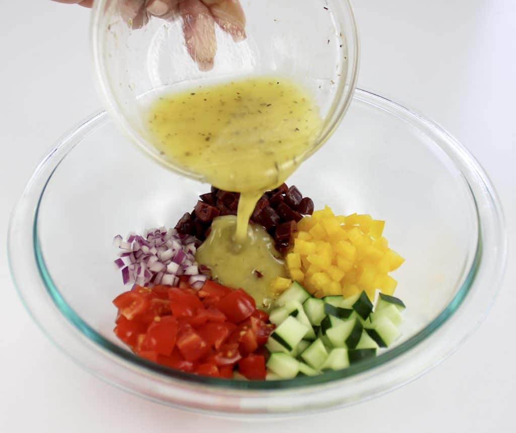 lemon dressing being poured over chopped veggies in glass bowl