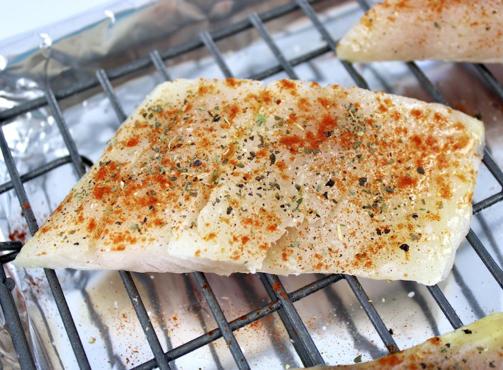 closeup of raw red snapper with spices on top on baking rack