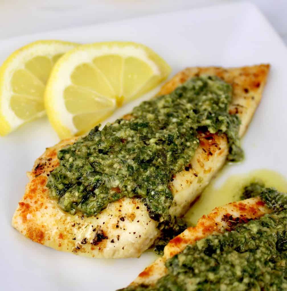 red snapper with pesto sauce on top with lemon slices on white plate
