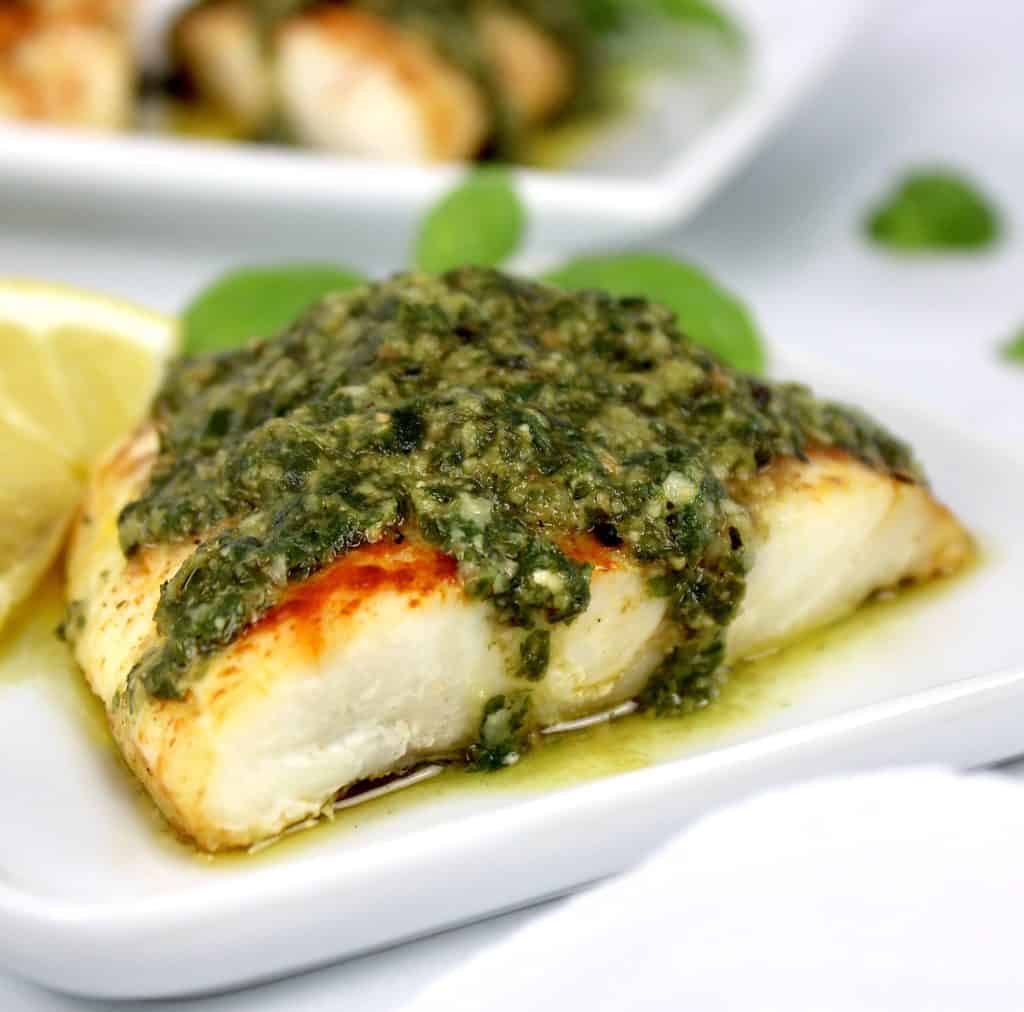 closeup of red snapper with pesto sauce on top slice of lemon on side