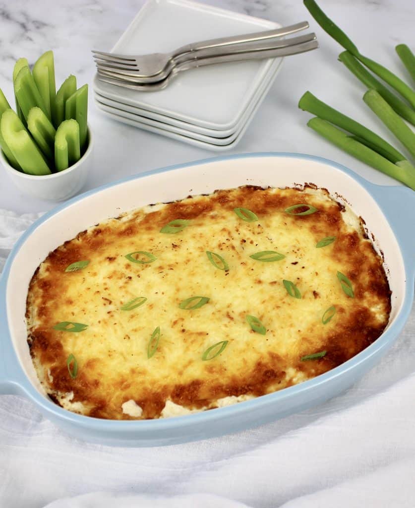 Crab Rangoon Dip in casserole dish with celery and scallions on background