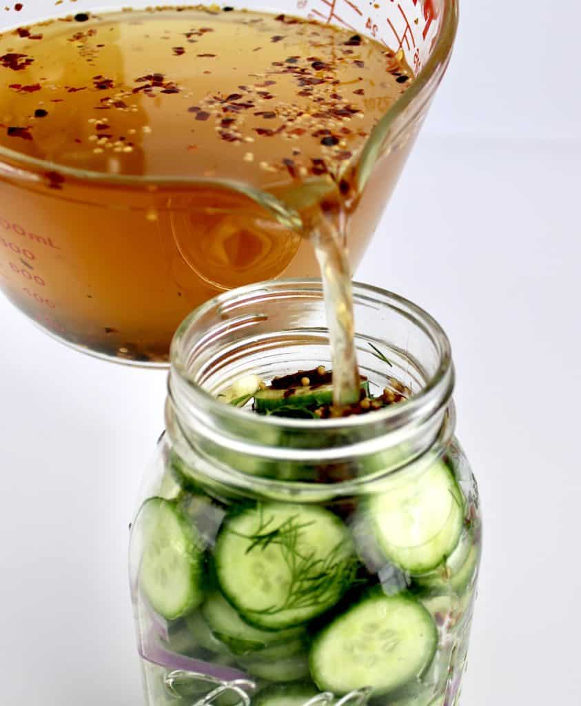 pickle brine being poured into jar of cucumber slices