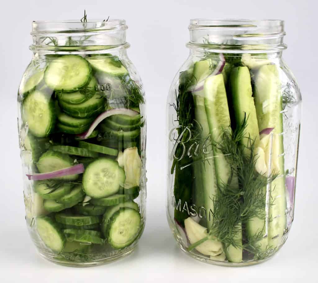 side view of 2 mason jars with sliced cucumber and cucumber spears garlic dill and onions