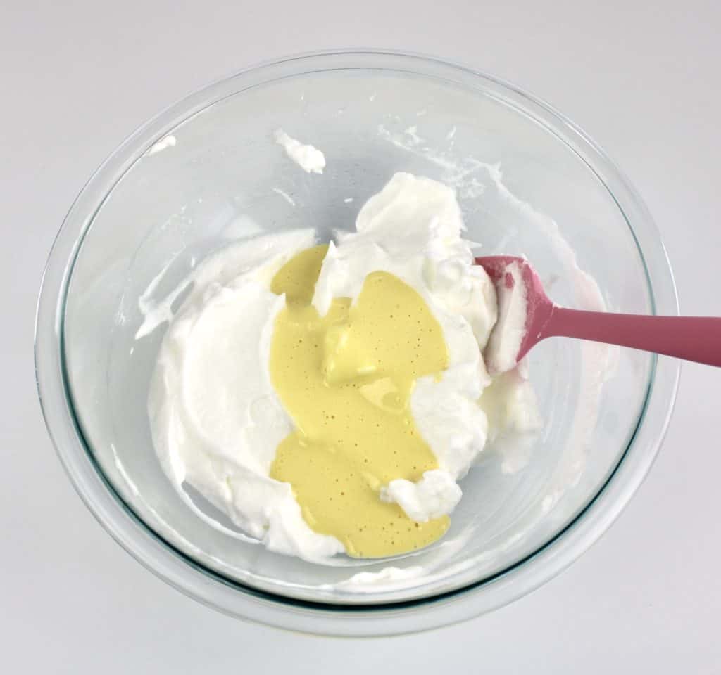 egg yolks on top of beaten egg whites in glass bowl with pink spoon