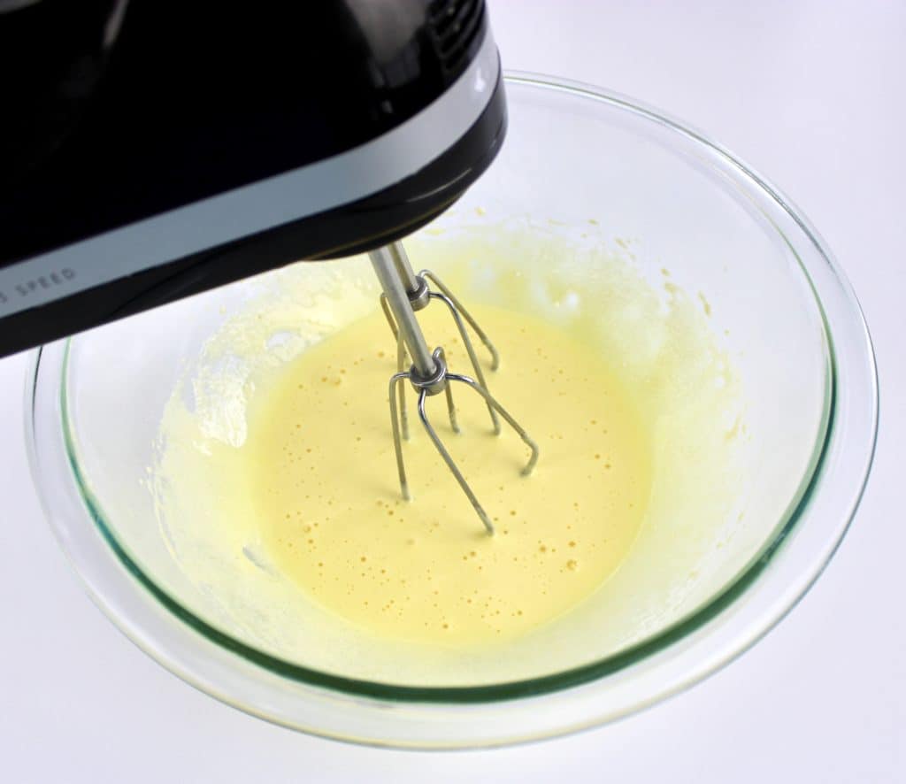 egg yolks being mixed with hand mixer in glass bowl