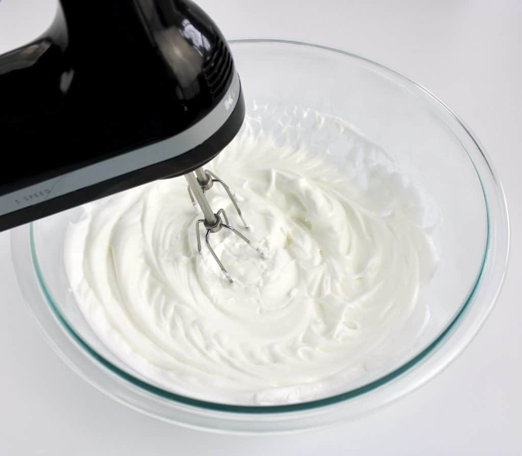 egg whites being mixed with hand mixer in glass bowl